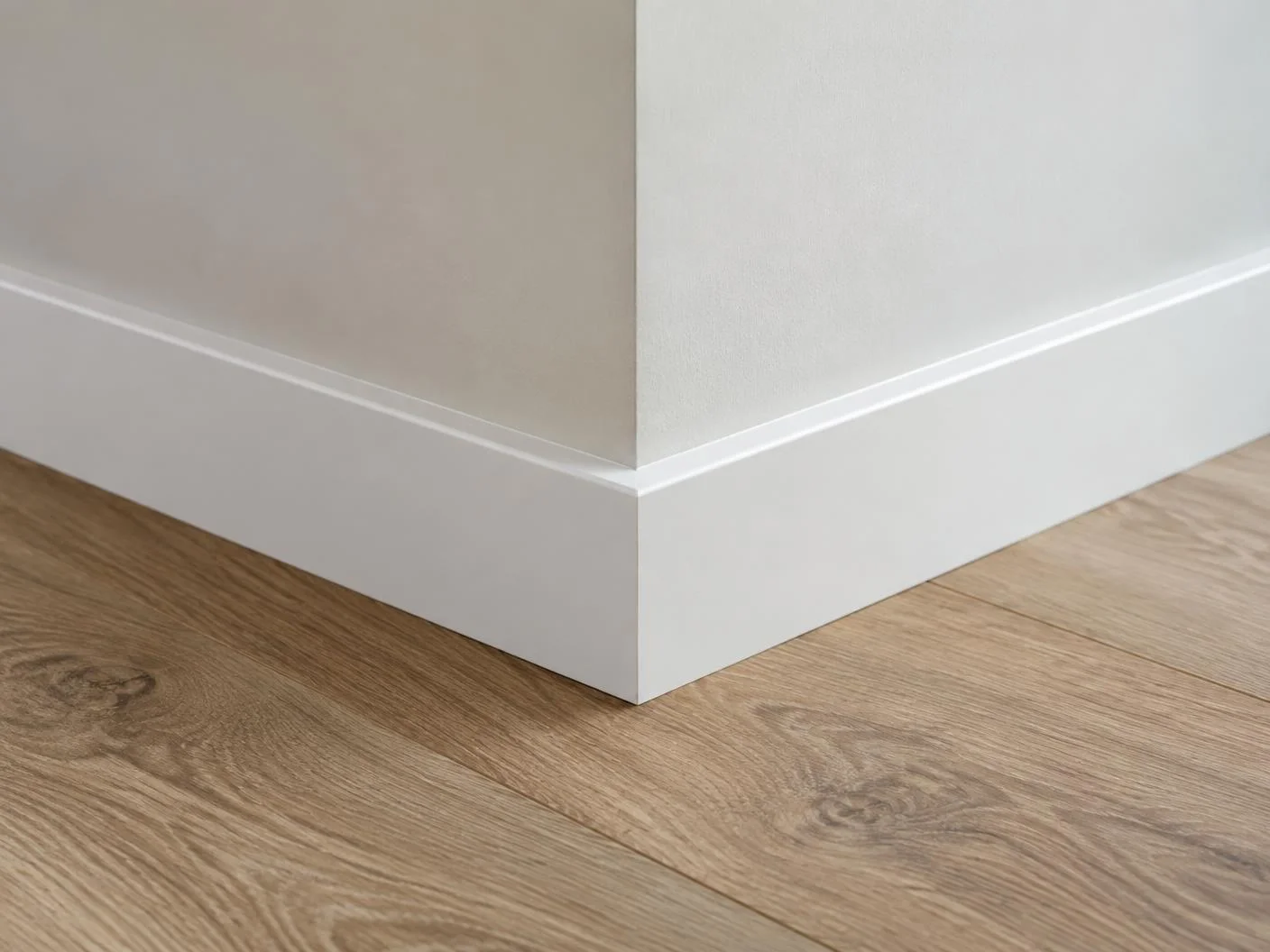 Rodapé branco instalado sobre piso laminado em canto de parede