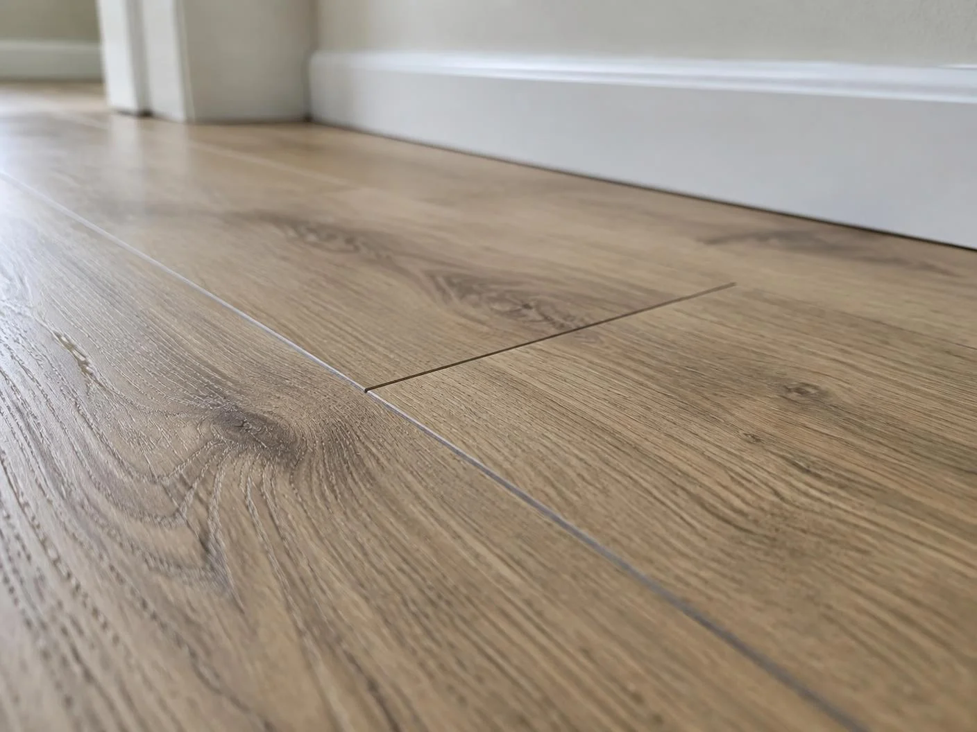 Detalhe das réguas de piso laminado tom carvalho natural com rodapé branco